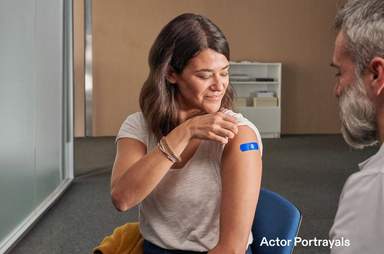 Actor portrayal of an adult male doctor looking at a woman with her sleeve rolled up with a Pfizer band aid on her arm