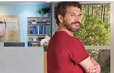 Actor portrayal of an adult man at least 19 years of age smiling with arms crossed with doctors office and woods in the background