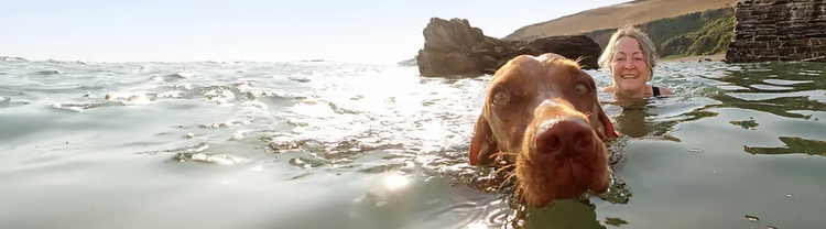 Older woman swimming in a lake with a brown dog