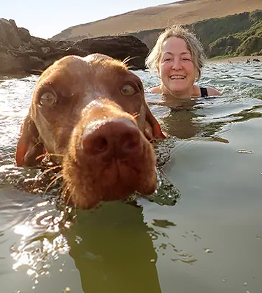 Older woman swimming in a lake with a brown dog